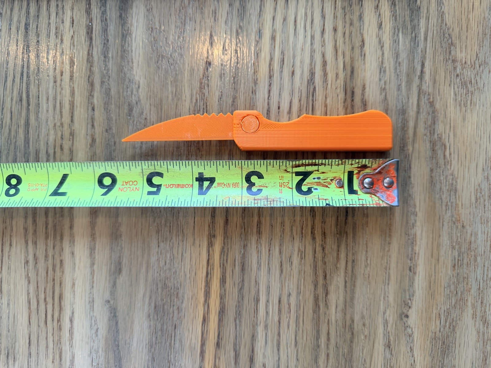 Actual orange Clicknpickit pocket tool beside an inch-marked tape measure